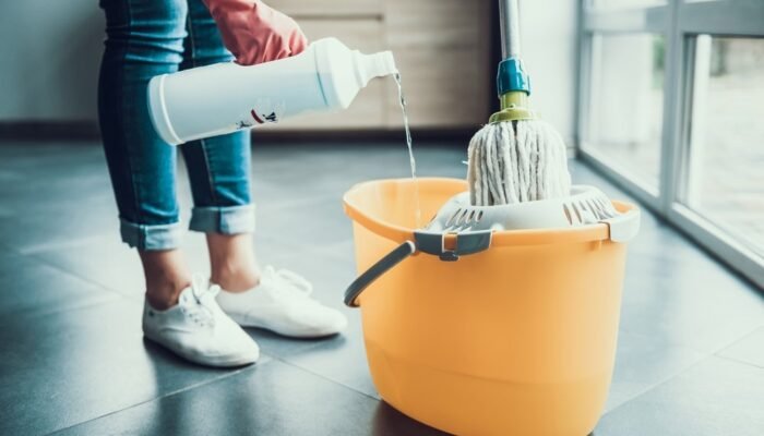 Woman in Gloves prepearing to Wipe Floor with Mop. Closeup of Girl wearing Protective Gloves mixing Cleaning products with water in Bucket with Mop. Woman Cleaning Apartment